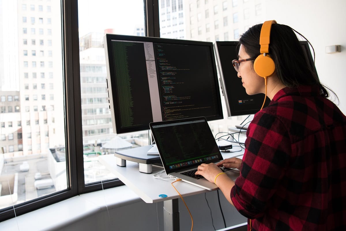 Female computer developer sitting at desk in front of three screens. 