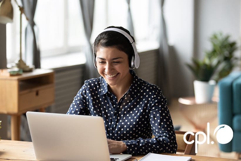 Smiling female wearing headphones working remotely on her laptop. 