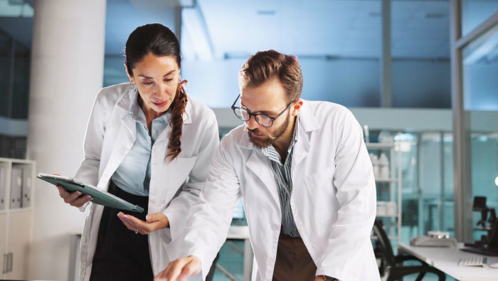 Two professionals in lab coats collaborate over a table, discussing data or findings in a modern laboratory setting.