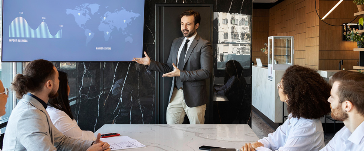 Cpl professional giving a presentation to a team in a modern office with a large screen displaying data and world market insights