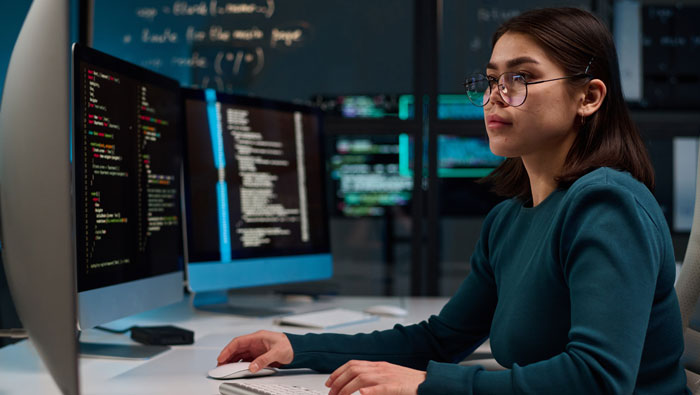 A focused individual working at a desk with multiple monitors displaying code and data in a tech environment.
