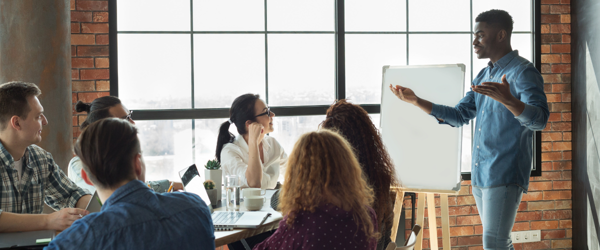 Group of colleague sitting at a table looking at male presenting